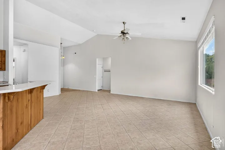 Vaulted ceiling with a ceiling fan, tiled flooring, wood-finish breakfast bar, and a large window