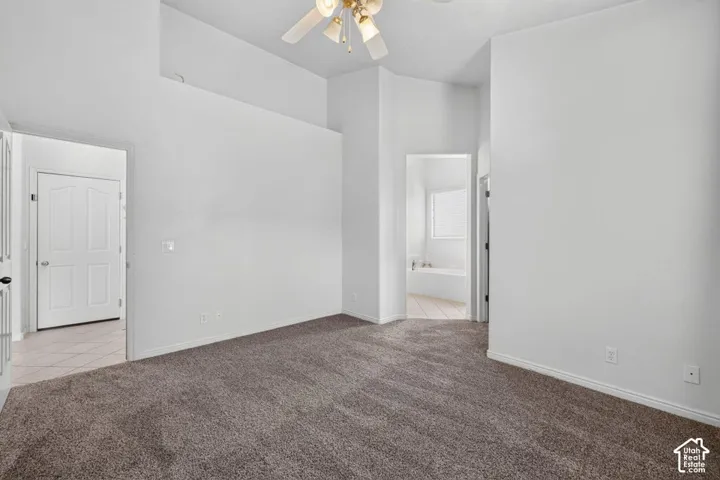 Vaulted ceiling with ceiling fan, carpeted flooring, and a doorway leading to a tiled room with a soaking tub