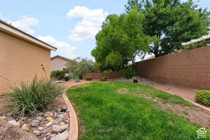 Expansive backyard featuring a green lawn, concrete curbing, and a block perimeter wall