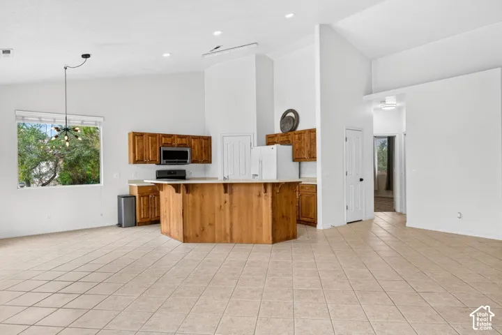 Spacious open-concept living area featuring high vaulted ceilings, large window, tile flooring, and a kitchen island with wood-finish cabinetry