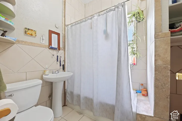 White pedestal sink, ceramic tile flooring, and fully tiled shower surround with a built-in window