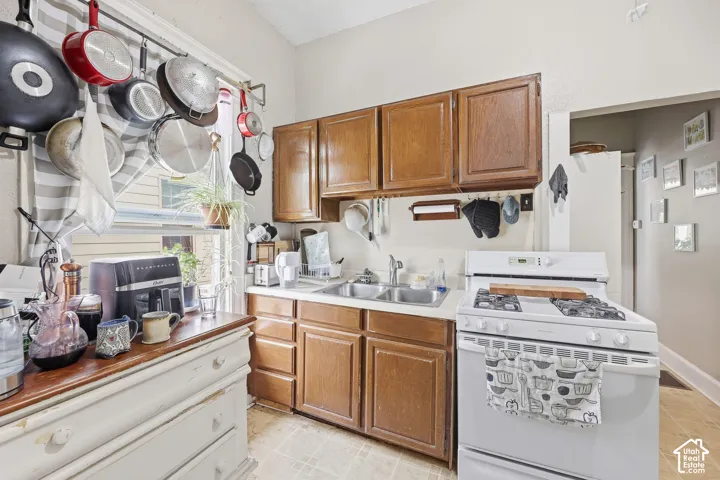 Kitchen featuring wood cabinetry, a double basin stainless steel sink, a gas range, and a refrigerator