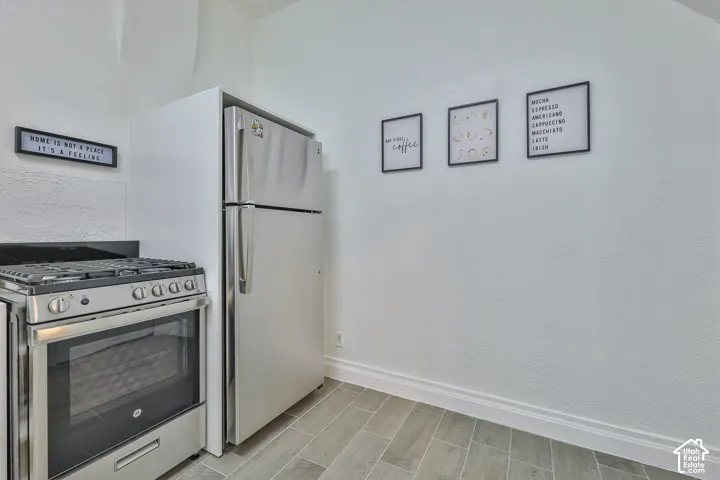 Modern kitchen featuring stainless steel appliances including a dual-fuel range with convection oven and a refrigerator with freezer, neutral tile flooring, and white painted walls with framed motivational décor