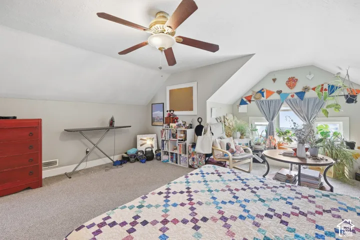Angled ceilings, ceiling fan with light fixture, carpeted flooring, wall-mounted shelving unit, and multiple windows