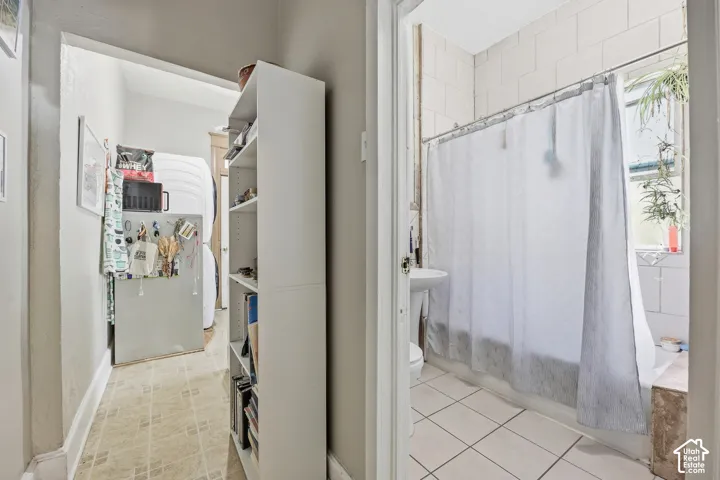Tiled flooring in a dedicated laundry area with built-in shelving, complemented by a separate bathroom featuring a pedestal sink, tiled shower surround, and a window