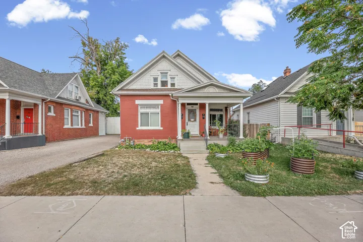 Red brick exterior with white trim, covered front porch, gabled roofline, and established front yard landscaping