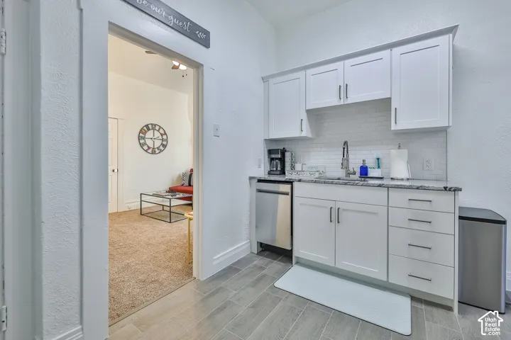 Kitchenette featuring white cabinetry, a stainless steel dishwasher, a single-basin sink with a gooseneck faucet, a light-toned backsplash, and a stone-finish countertop