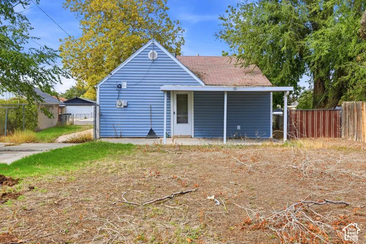 Rear exterior featuring blue vinyl siding, covered patio, and mature trees