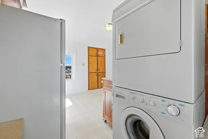 Stackable washer and dryer, white refrigerator, light-colored flooring, white walls, and built-in wood-finish cabinetry