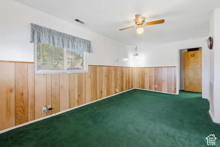 Room featuring wood paneling, a ceiling fan, a window with blinds, and green carpeting