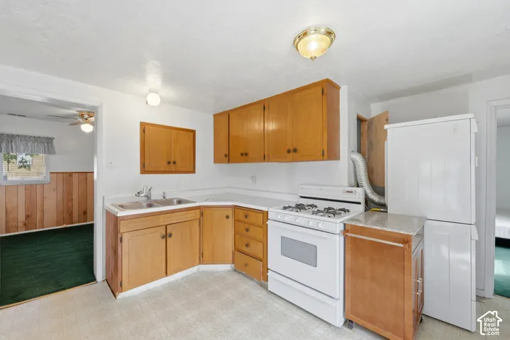 Efficient kitchen layout featuring warm wood cabinetry, white gas range with oven, stainless steel refrigerator, undermount sink with faucet, and tile flooring