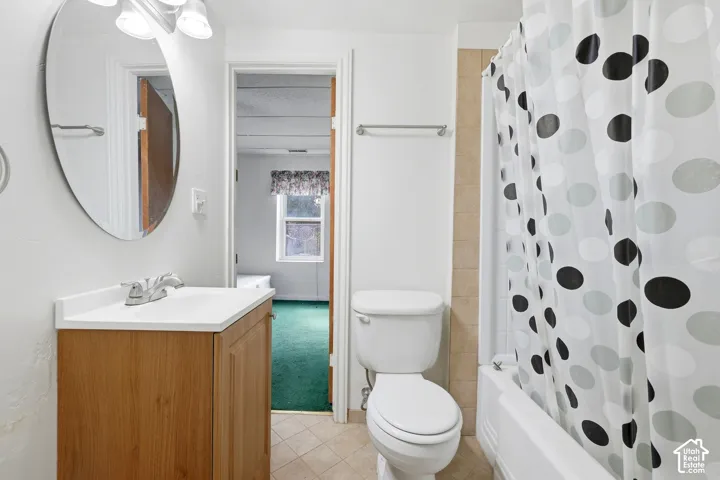 Bathroom featuring a wood-finish vanity with a white countertop and integrated sink, a rounded wall-mounted mirror, a two-piece toilet, and a bathtub with tiled surround