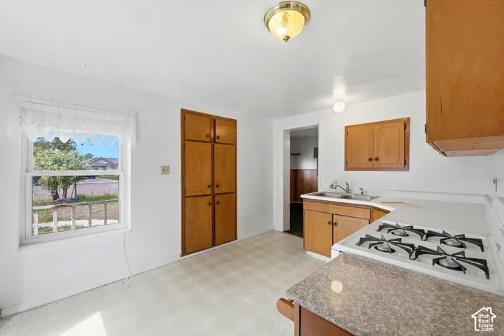 Bright kitchen featuring wood-finish cabinetry, gas cooktop, undermount sink, and neutral tile flooring