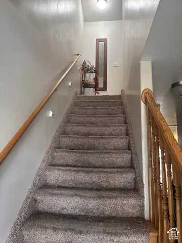 Carpeted staircase featuring a wood handrail and balusters, with a ceiling-mounted light fixture