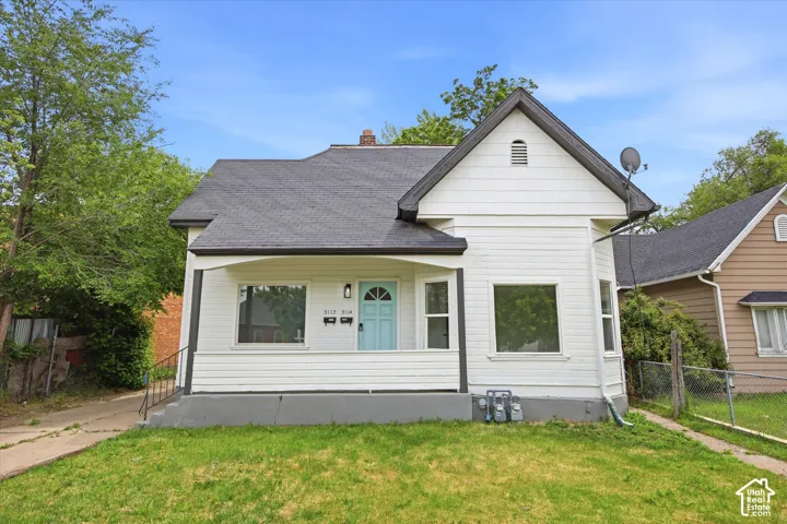 White siding exterior with a contrasting dark roof, covered porch entrance with a light blue door, and front yard with green grass