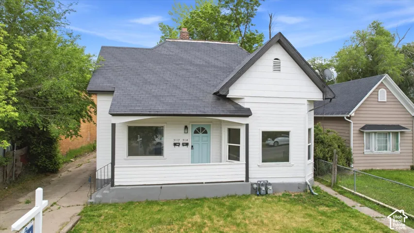White siding exterior with a dark shingle roof, featuring a light blue front door and a covered porch