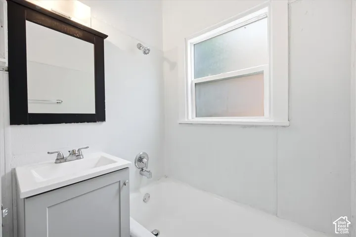 Bathroom with a window, white bathtub, vanity with integrated sink, and wall-mounted mirror