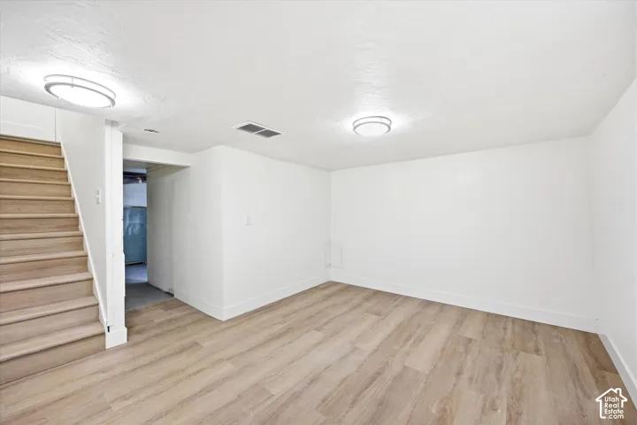 Light wood-finish flooring, white painted walls, recessed lighting, and a finished staircase