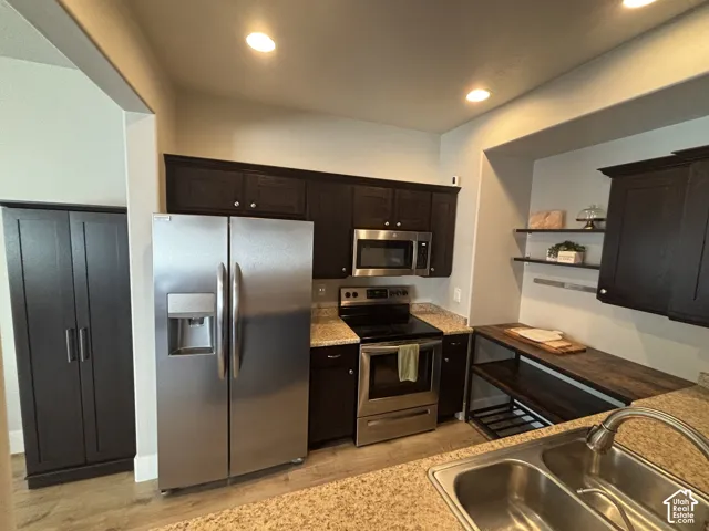 Kitchen featuring dark wood-finish cabinetry, stainless steel appliances, speckled stone-finish countertops, and wood-finish flooring