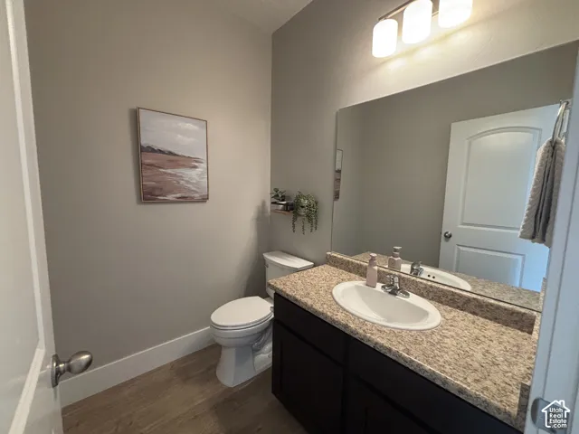 Powder room featuring a single vanity with an integrated sink, a speckled countertop, dark wood-finish cabinetry, and wood-finish flooring