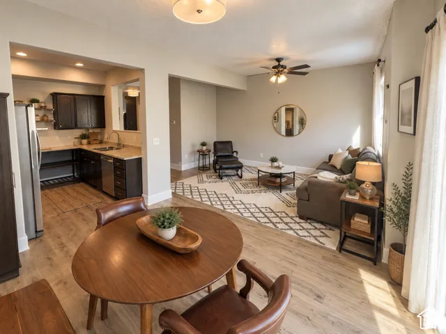 Open-concept living area featuring wood-finish flooring, a kitchen with dark cabinetry and light countertops, and a ceiling fan