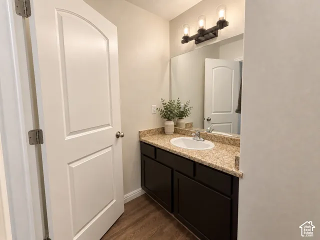 Wood-finish flooring, dark wood vanity with ample storage, integrated sink, speckled countertop, and a three-light fixture