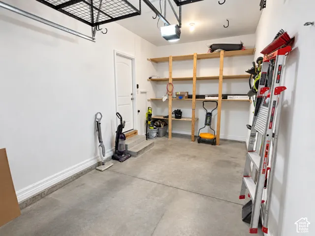 Attached overhead storage rack, concrete flooring, built-in wooden shelving, and a white access door