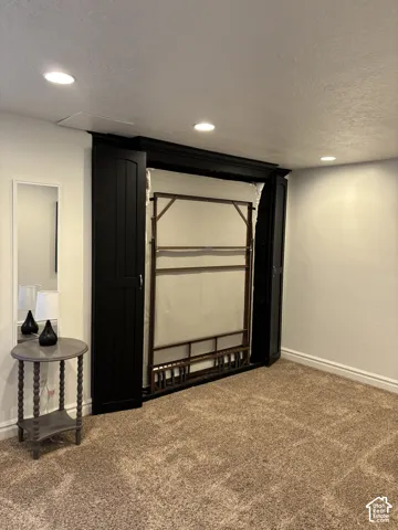 Recessed lighting illuminates the space, featuring a built-in Murphy bed with dark cabinetry, and neutral-toned carpet flooring