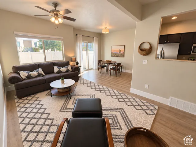 Open-concept living space with wood-finish flooring, a ceiling fan, and a dining area with a drum pendant light