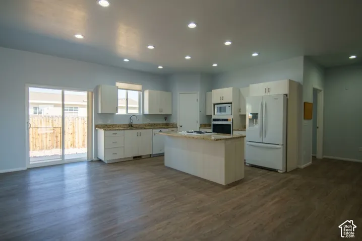 Kitchen featuring a center island, wood-finish flooring, recessed lighting, white cabinetry, and granite-style countertops