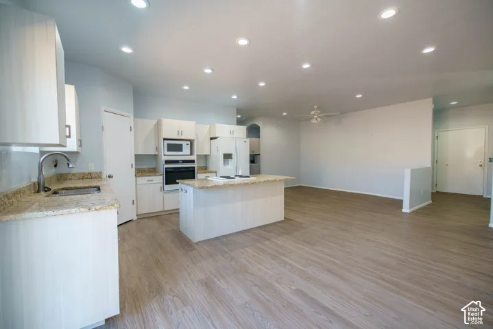 Kitchen and living area featuring wood-finish flooring, recessed lighting, ceiling fan, and white cabinetry