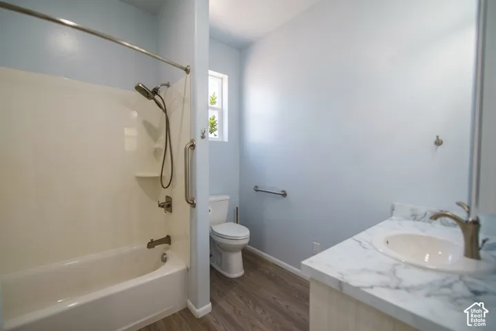 Integrated bathtub and shower combination with a handheld showerhead, a single-sink vanity with a marble-patterned countertop, and wood-finish flooring