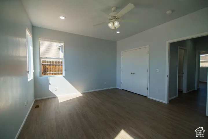 Room featuring wood-finish flooring, two windows with white blinds, a ceiling fan with integrated lighting, and a closet with bi-fold doors