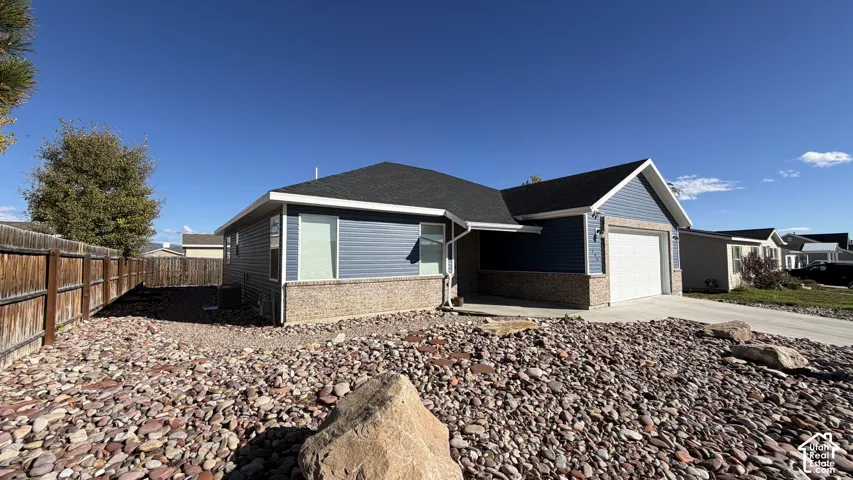 Single-story residence featuring blue horizontal siding, stone veneer accents, an asphalt shingle roof, a concrete driveway, and a fenced yard with rock landscaping
