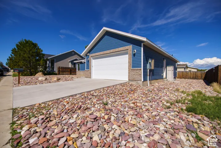 Blue siding exterior with brick veneer accents, an attached garage, a concrete driveway, and rock landscaping
