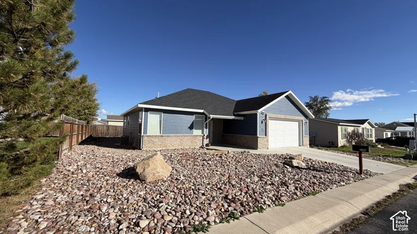 Single-level exterior featuring blue horizontal lap siding, masonry veneer base, asphalt shingle roofing, and a concrete driveway leading to an attached two-car garage