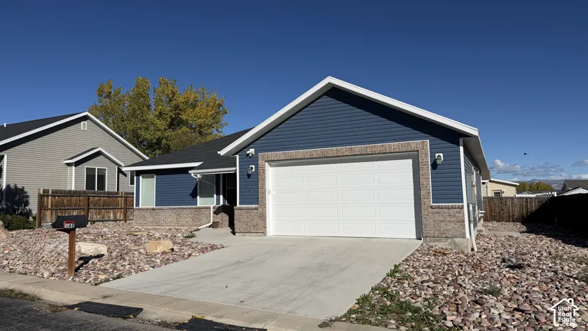 Single-story exterior featuring blue horizontal siding, stone veneer accents, an attached two-car garage, and low-maintenance rock landscaping