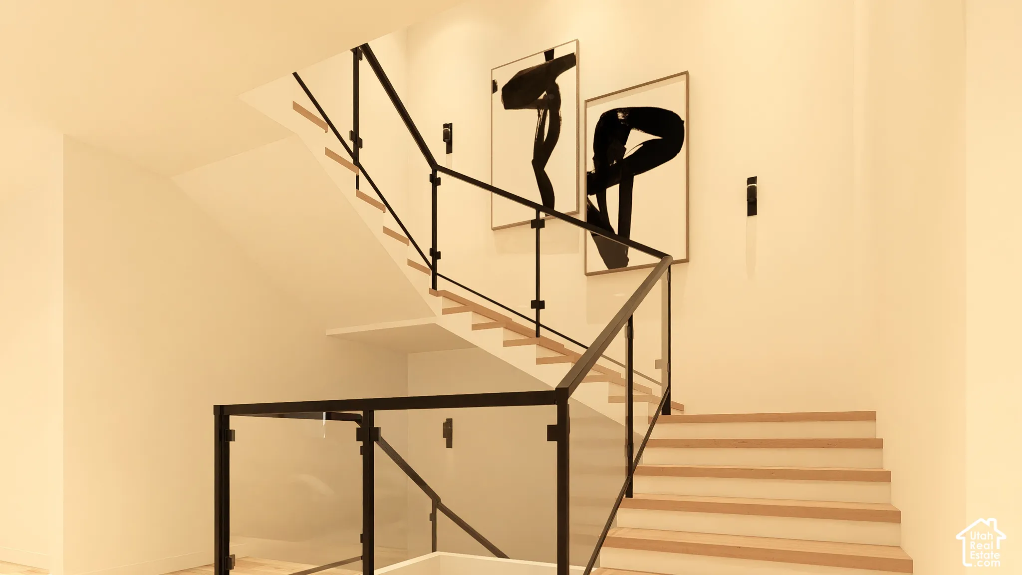Open staircase featuring light wood treads, white risers, and contemporary glass and black metal railings
