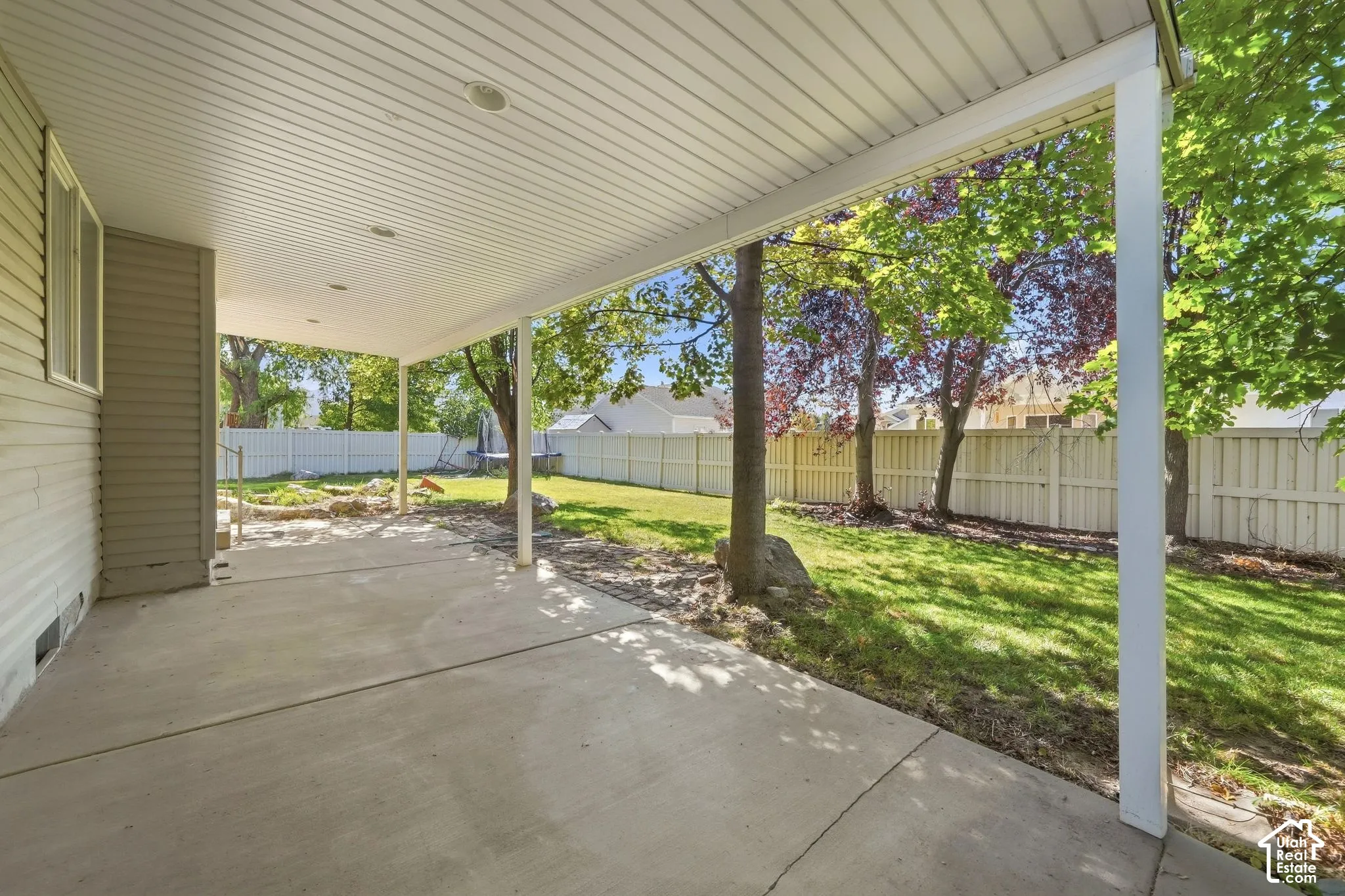 Expansive concrete patio with a covered overhead structure, recessed lighting, and a durable vinyl fence