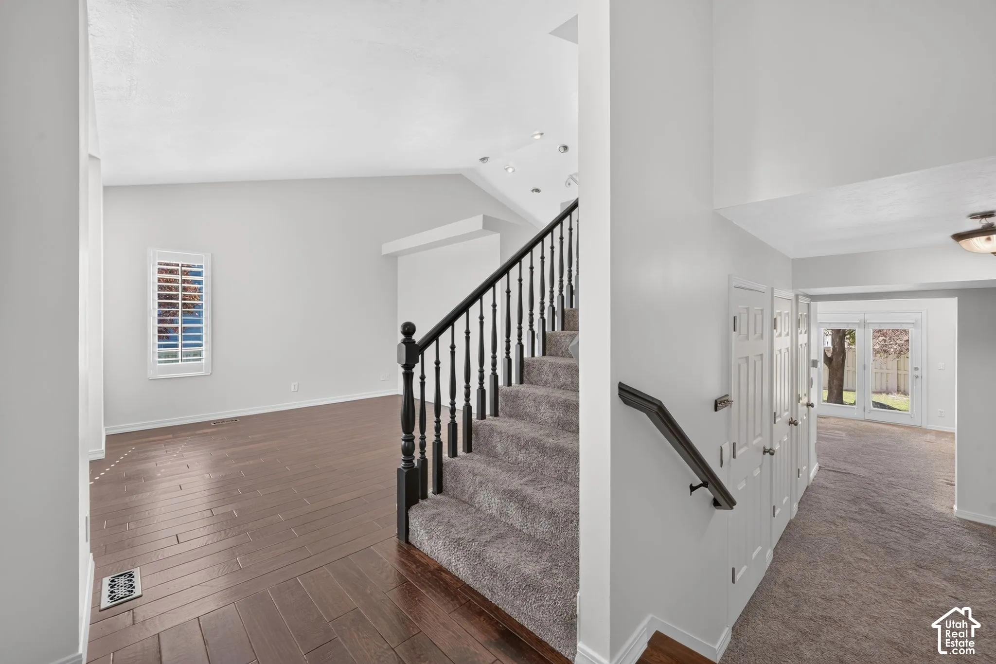 Two-story entryway with a vaulted ceiling, wood-finish flooring, a carpeted staircase with dark wood newel posts and spindles, and a window with plantation shutters