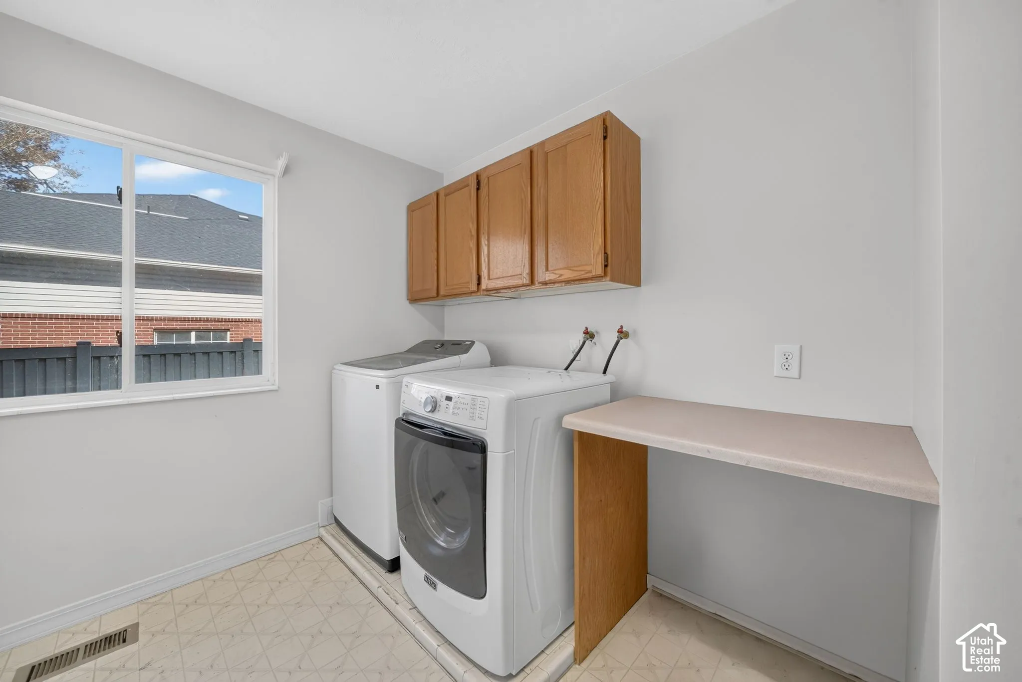 Light-filled utility space featuring upper wood cabinetry, a built-in countertop, and a window
