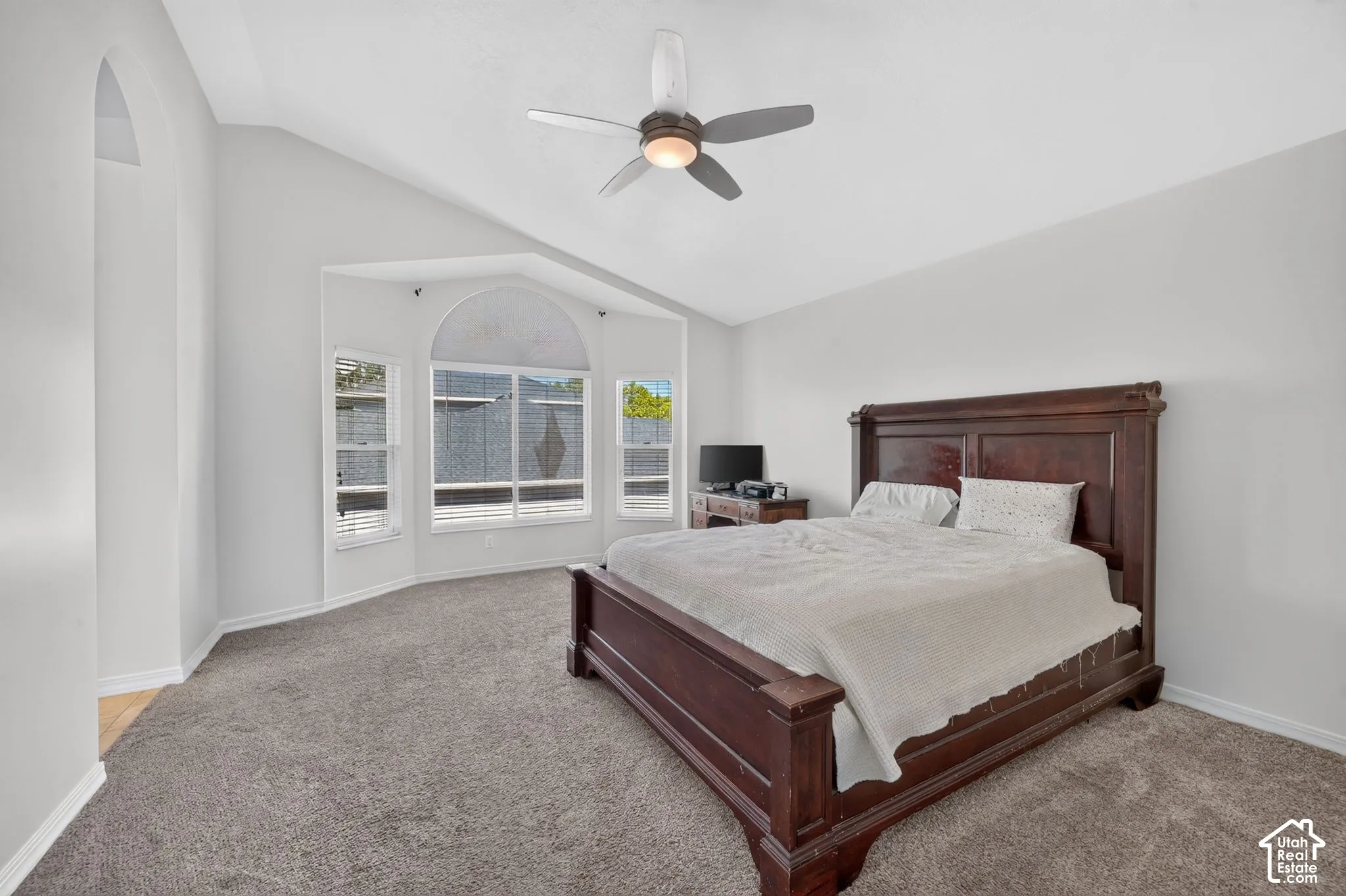 Vaulted ceiling with ceiling fan, arched wall niche, bay window with arched transom, and carpeted flooring