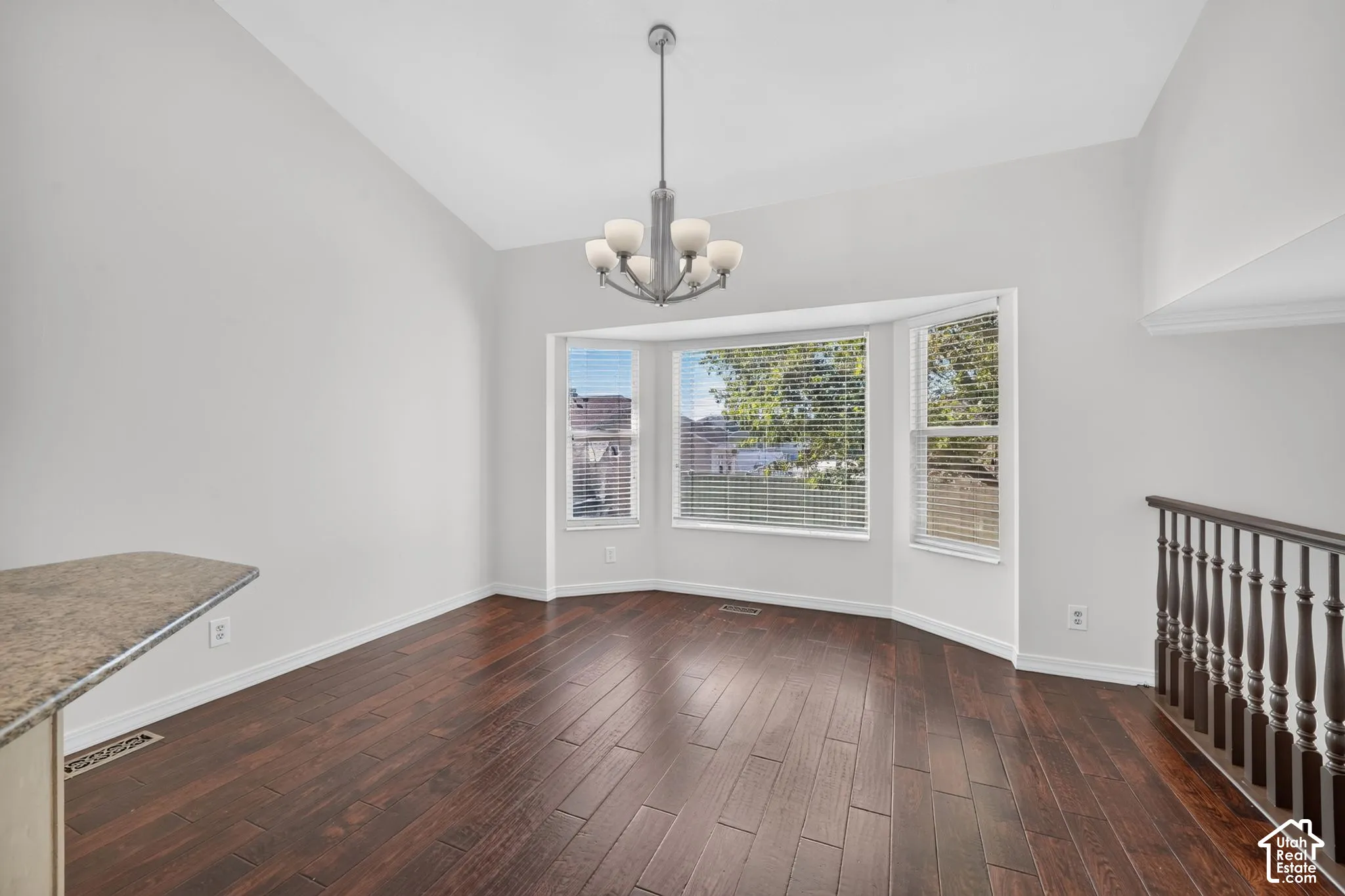 Vaulted ceiling with a chandelier, bay window with blinds, wood-finish flooring, and a stone-finish countertop