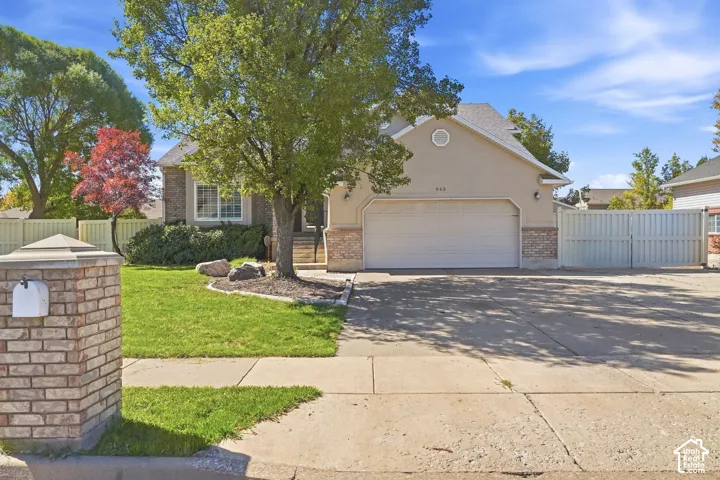Stucco and brick facade with an attached two-car garage, mature landscaping, and a paved driveway