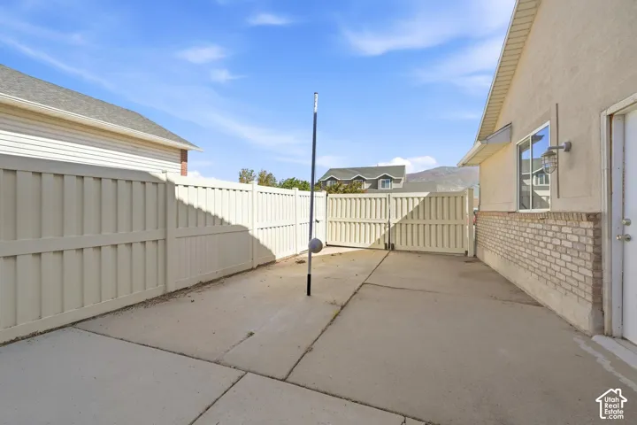 Paved patio area featuring privacy fencing, exterior lighting fixture, and a brick veneer facade