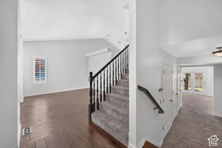 Two-story entryway with a vaulted ceiling, wood-finish flooring, a carpeted staircase with dark wood newel posts and spindles, and a window with plantation shutters