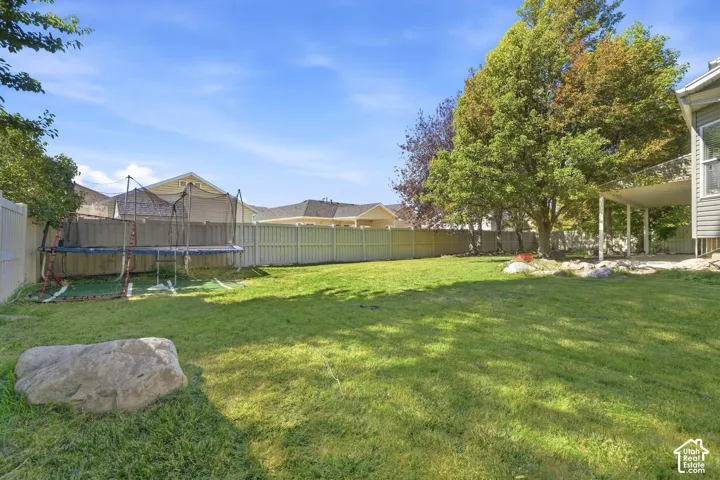 Expansive grass lawn with mature trees, a covered patio, and perimeter fencing