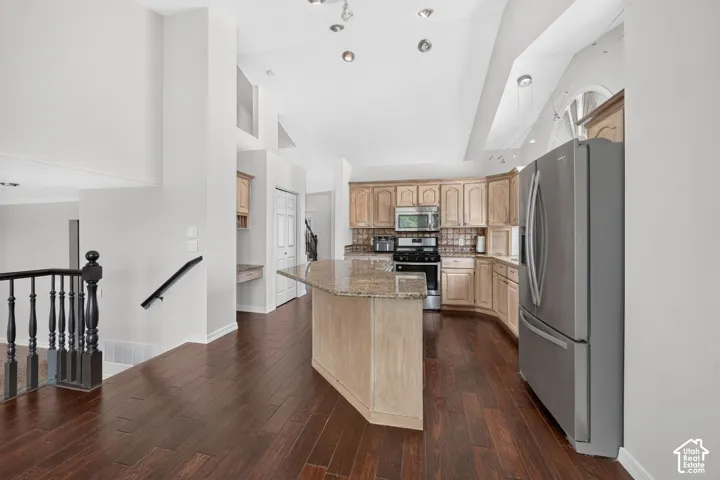 Kitchen featuring wood-finish flooring, a kitchen island with stone countertop, wood cabinetry, and stainless steel appliances