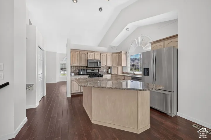 Kitchen featuring a central island with a granite countertop, wood-finish flooring, vaulted ceiling, and stainless-steel appliances