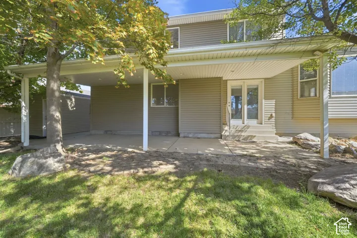 Covered patio with concrete flooring, dual glass-paneled exterior doors, and a partial grass lawn
